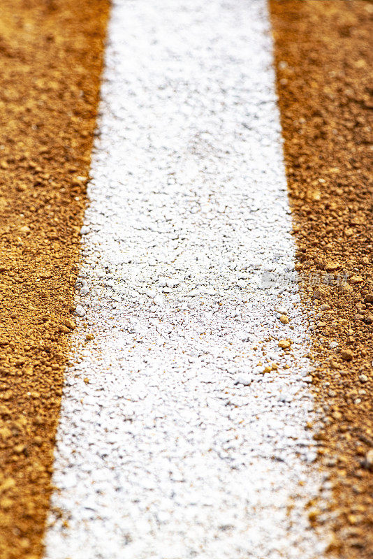在棒球/垒球场地的泥土上，一条白色的公平/犯规线的特写